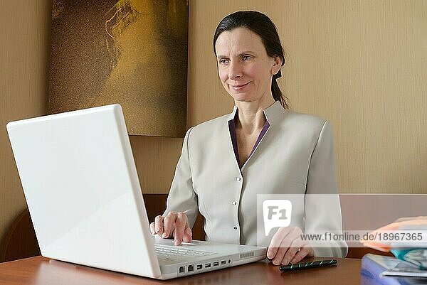 Eine elegante Geschäftsfrau arbeitet mit einem Laptop. Sie ist zufrieden mit ihrer Arbeit