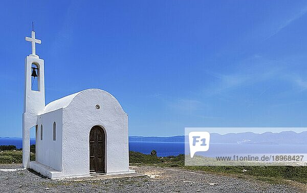 Weiße griechisch orthodoxe Kapelle oder Kirche auf einem Hügel an der Meeresküste gegen einen klaren blauen Himmel an einem sonnigen Tag. Traditionelles religiöses Gebäude. Typische griechische Landschaft. Diagonale Komposition  Kopierraum