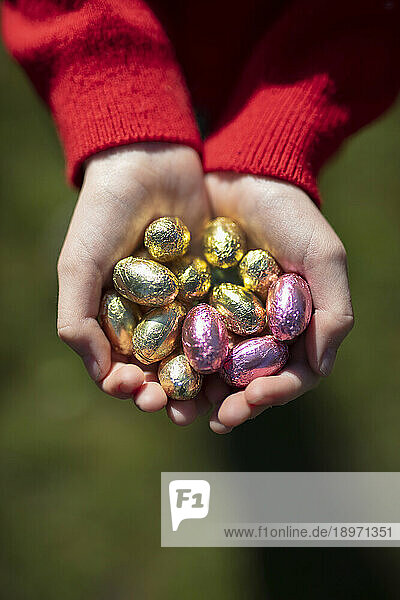 Children's hands holding lots of little wrapped chocolate Easter eggs