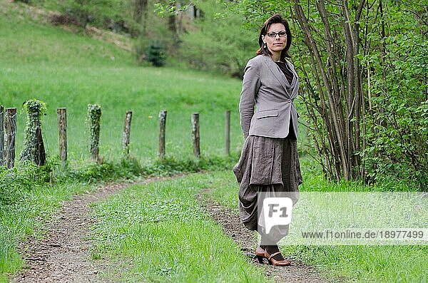 Elegante Frau  die auf einem Waldweg in der Nähe eines Zauns steht
