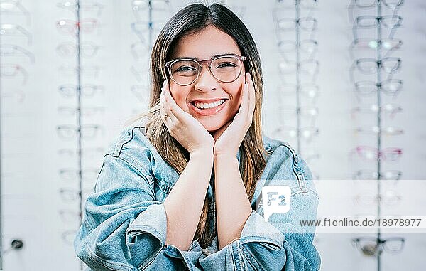 Glückliches Mädchen modelliert eine Brille in einem Geschäft für optische Linsen. Porträt eines schönen Mädchens  das in einem Optikgeschäft eine Brille modelliert