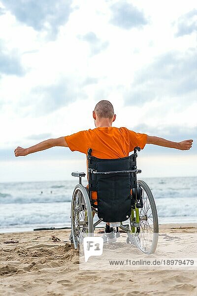Eine behinderte Person auf dem Rücken in einem Rollstuhl am Strand fühlt sich frei