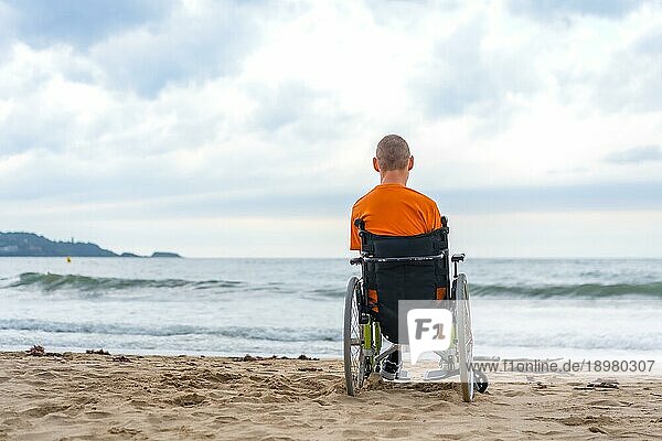 Ein Behinderter in einem Rollstuhl auf dem Rücken am Strand im Sommer mit Blick auf das Meer