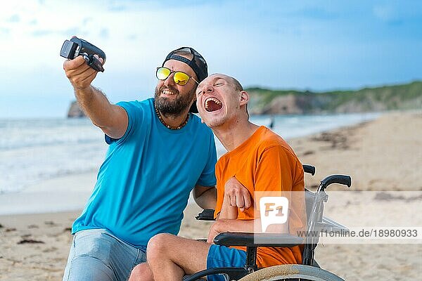 Eine behinderte Person im Rollstuhl am Strand mit einem Freund  der Spaß daran hat  ein Selfie zu machen