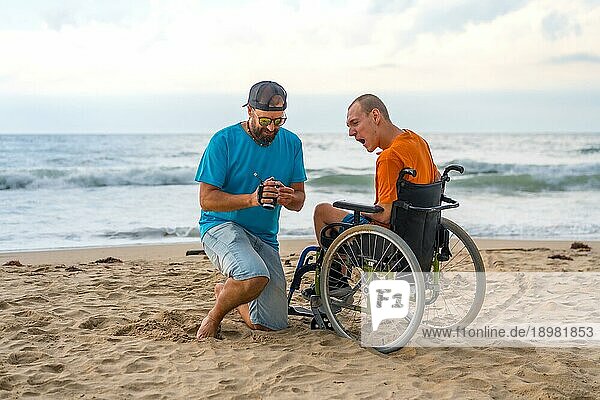 Eine behinderte Person im Rollstuhl am Strand  die sich mit einem Freund und einer Videokamera amüsiert