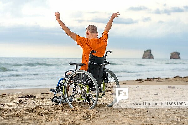 Eine behinderte Person auf dem Rücken in einem Rollstuhl am Strand mit offenen Armen  die die Freiheit des Meeres und der Natur genießen