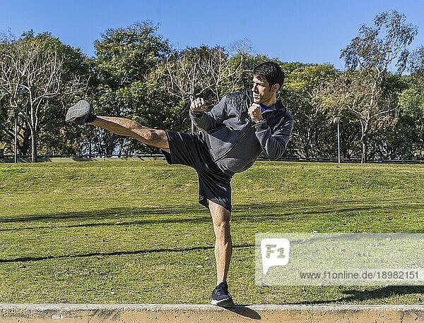 Junger athletischer Kampfsportler  der in einem öffentlichen Park Kicks übt