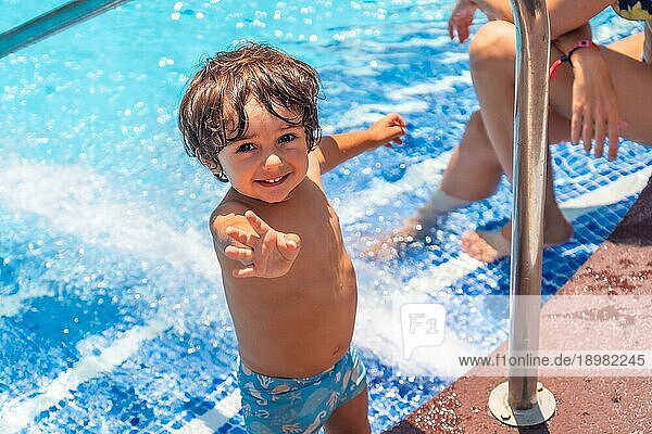Zweijähriger Junge  der den Sommer im Schwimmbad genießt und lächelnd in die Kamera schaut