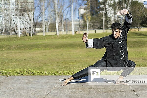 Junger athletischer Kampfsportler in klassischer Kung Fu Uniform  der in einem öffentlichen Park Kicks übt. Raum kopieren