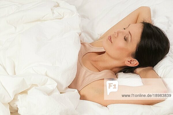 Gesunde  verjüngte junge Frau  die sich im Bett zwischen ihre Kissen kuschelt  die Arme hinter dem Kopf verschränkt