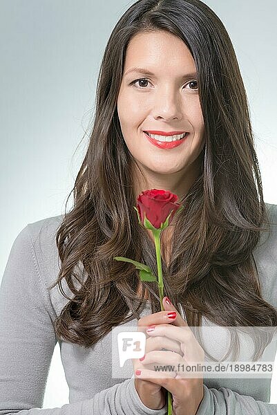 Attraktive Frau mit langem brünetten Haar hält eine langstielige rote Rose  ein Geschenk von einem geliebten Menschen zum Valentinstag oder Geburtstag