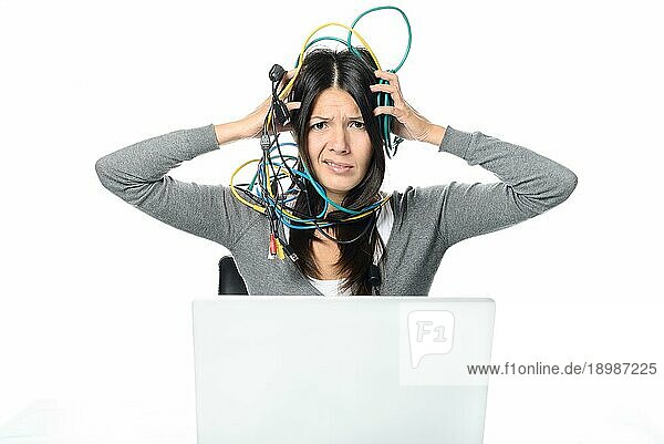 Nahaufnahme Verärgerte Frau in grauem langärmeligem Hemd  die sich verworrene Netzwerkkabel auf den Kopf legt  während sie keine Internetverbindung zu ihrem Laptop hat. Schaut in die Kamera. vor weißem Hintergrund