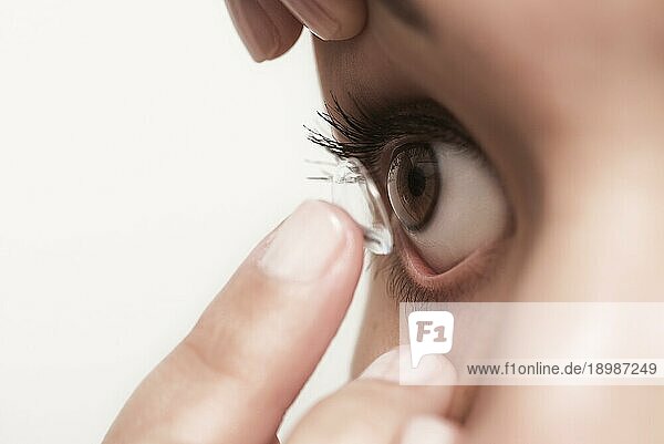 Eine Frau  die eine Einweg Kontaktlinse aus Kunststoff in ihr Auge einsetzen will  um ihre Sehkraft zu korrigieren  balanciert diese auf dem Ende ihres Fingers vor ihrem Auge  mit Blick auf das Auge  extreme Nahaufnahme