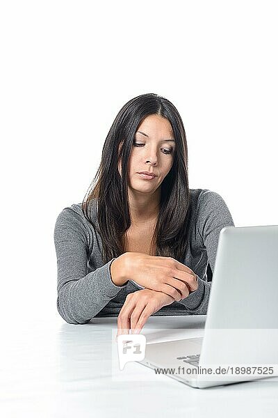 Gelangweilte attraktive junge Büroangestellte  die an ihrem Laptop sitzt und auf ihre Uhr schaut  um zu sehen  ob es Zeit ist  nach Hause zu gehen  auf weißem Grund
