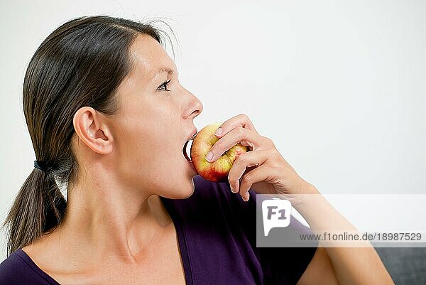 Seitenansicht einer attraktiven jungen Frau  die in einen frischen  saftigen  roten Apfel beißt  da sie eine gesunde Ernährung und Lebensweise verfolgt
