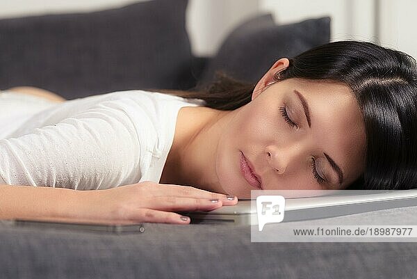 Attraktive junge Frau  die ihren Kopf mit geschlossenen Augen auf einem Laptopcomputer ruht und einen friedlichen Schlaf auf dem Sofa genießt