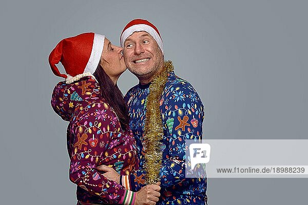 Zärtliches Paar mittleren Alters in festlicher  weihnachtlicher Kleidung  das sich umarmt und küsst  während es Weihnachten zusammen vor einem grauen Hintergrund in Seitenansicht feiert