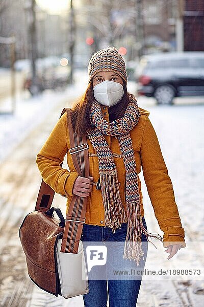 Brünette Frau mittleren Alters in Winterkleidung trägt auf dem Weg zur Arbeit eine Gesichtsmaske wegen des Coronavirus im Freien