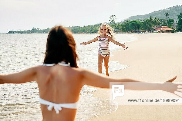 Glückliches kleines Mädchen läuft zu ihrer Mutter für Umarmungen am tropischen Strand. Sommerurlaub  glückliche Familie  Liebe Konzept