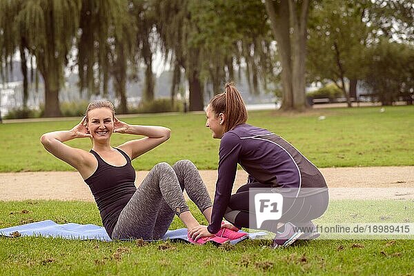 Glückliche sportliche Frau  die in die Kamera lächelt  während sie im Park mit Hilfe ihres Freundes Lockenübungen macht