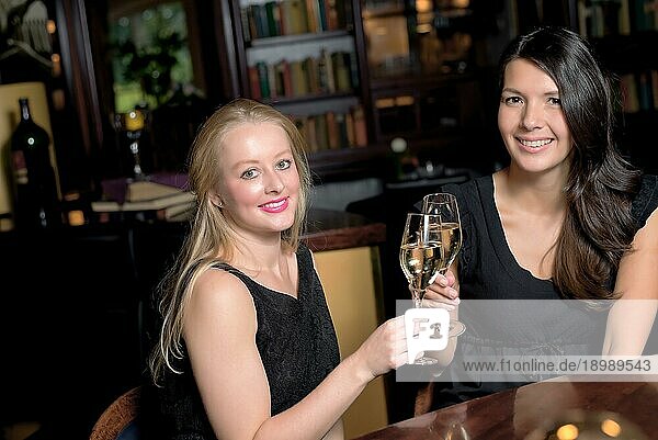 Zwei schöne elegante Frauen Freunde in stilvollen einfachen schwarzen Cocktailkleider Toast einander mit Gläsern von gekühlten Champagner  wie sie auf eine Nacht zusammen feiern
