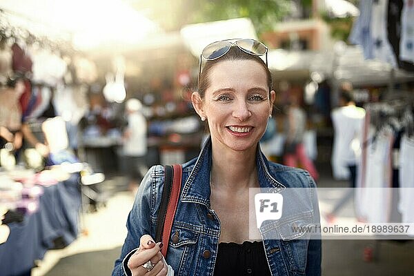 Glückliche  attraktive  stilvolle Frau  die auf einem Markt im Freien einkauft und mit einem breiten  warmen  freundlichen Lächeln in die Kamera schaut