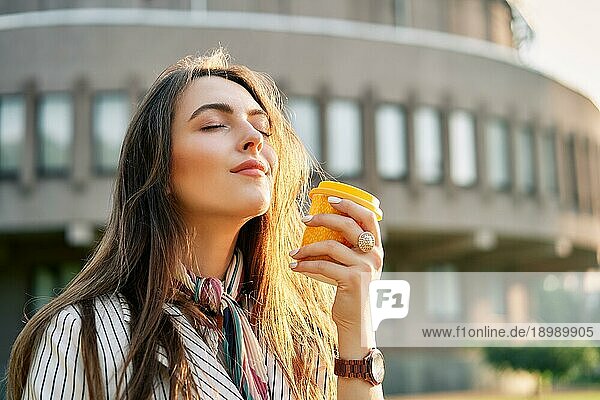 Junge stilvolle Frau auf der Straße trinkt Morgenkaffee im Sonnenlicht. Pause Zeit Konzept