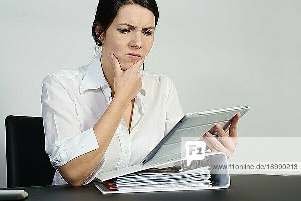 Eine verwirrte Frau  die angestrengt nachdenkt und eine Grimasse zieht  während sie versucht  eine Antwort auf ein Problem zu finden  das ihr auf ihrem Tabletcomputer gestellt wird