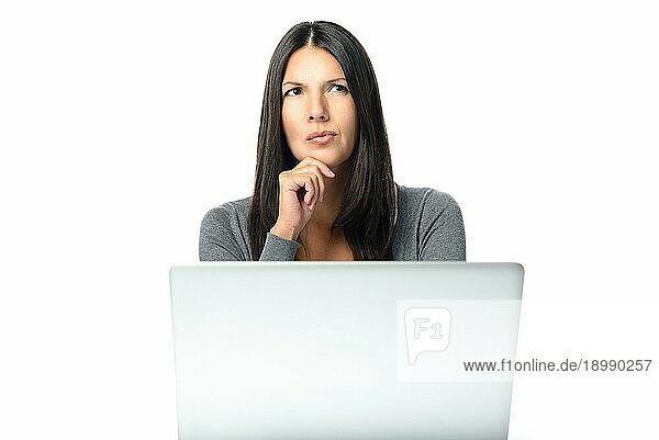 Attraktive  stilvolle  junge Geschäftsfrau mit einem besorgten Stirnrunzeln  die nachdenklich hinter ihrem Laptop an ihrem Schreibtisch sitzt und mit der Hand am Kinn und einem ernsten Gesichtsausdruck in die Luft starrt