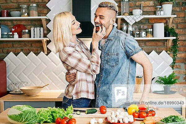 Schönes junges Paar füttert sich gegenseitig und lächelt beim Kochen in der Küche zu Hause. vegetarisch  Beziehung Konzept