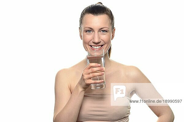 Hübsche junge Frau  die ein Röhrentop trägt und ein Glas Wasser in der Hand hält  während sie in die Kamera lächelt  vor weißem Hintergrund