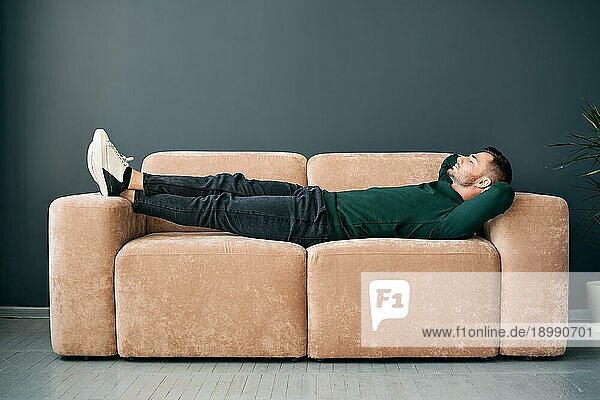 Junger trendiger Mann  der sich allein auf einem Textilsofa zu Hause entspannt. Ruhe Konzept