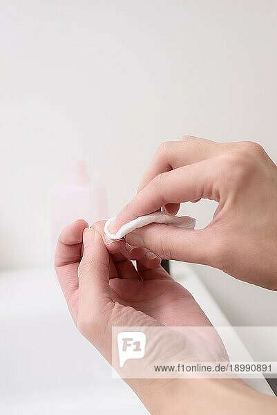 Frau entfernt Nagellack mit Aceton auf einem kleinen Wattepad auf dem Rand eines Handbeckens  während sie ihre Nägel und Nagelhaut in einem Gesundheits und Schönheitskonzept pflegt