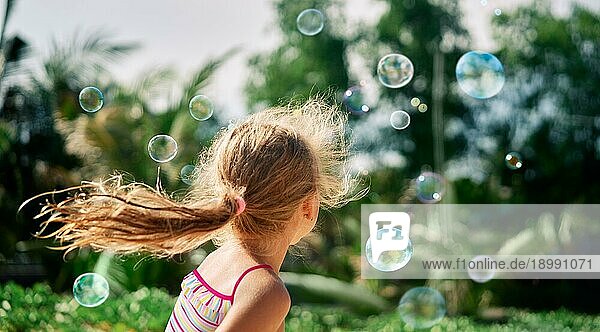 Rückansicht eines glücklichen kleinen Mädchens  das Seifenblasen in der Natur spielt. Kindheit  LifestyleKonzept