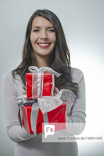 Hübsche junge Frau mit langen brünetten Haaren und einem schönen sanften Lächeln hält bunte rote Geschenke für einen geliebten Menschen aus