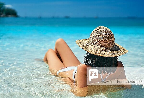 Rückenansicht der jungen Frau in Strohhut und weißem Bikini entspannen in türkisfarbenen Meer auf tropischen Paradies Strand. Sommerurlaub  Reiseziel  Urlaub Konzept