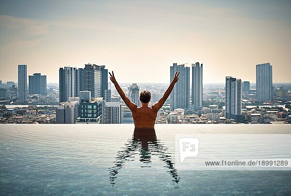 Zurück Blick auf glückliche Freiheit Mann mit erhobenen Armen genießen seinen Sommerurlaub am Swimmingpool auf dem Dach des Hotels. Reisen  Urlaub  Erfolg Konzept