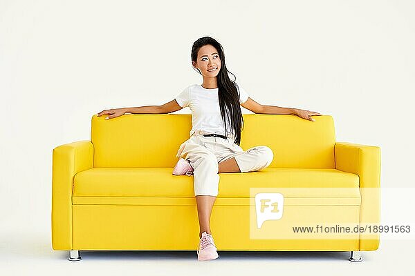 Hübsche lächelnde asiatische Frau entspannen auf gelber Couch auf weißem Hintergrund. Ruhe  Komfort Konzept