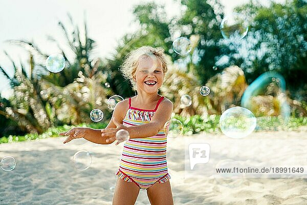 Kleines glückliches Mädchen spielt Seifenblasen am aktuellen Strand. Kindheit  LifestyleKonzept