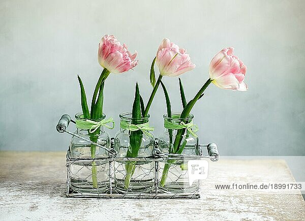 Drei zartrosa Tulpenblüten in kleinen Glasvasen mit dekorativem Tragekorb
