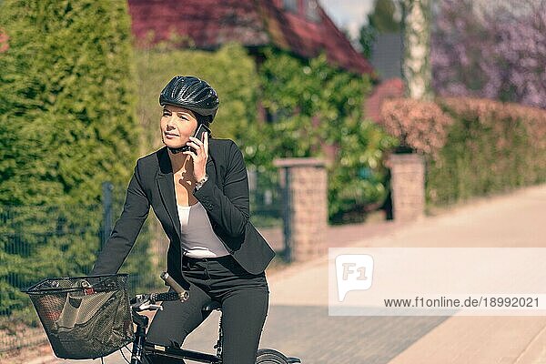 Aktive junge Geschäftsfrau  die auf ihrem Fahrrad fährt  während sie mit ihrem Mobiltelefon spricht