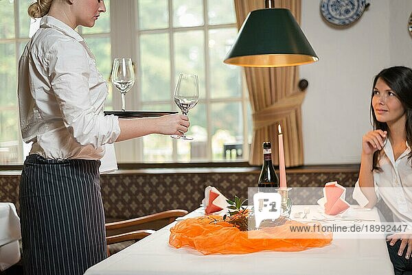 Eine weibliche Kellnerin serviert einer attraktiven jungen Frau in einem Restaurant Wein in eleganten Gläsern an einem formellen Tisch