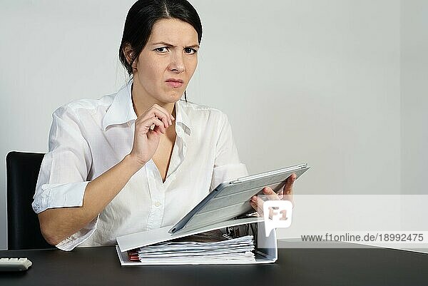 Eine verwirrte Frau  die angestrengt nachdenkt und eine Grimasse zieht  während sie versucht  eine Antwort auf ein Problem zu finden  das ihr auf ihrem Tabletcomputer gestellt wird