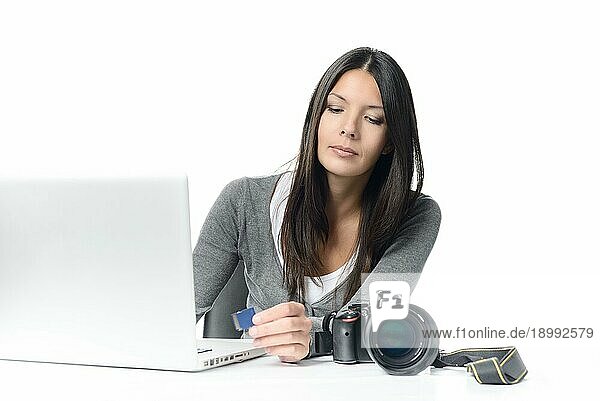 Ernsthafte junge Fotografin überträgt Bilddateien von der SD Karte auf den Laptop an ihrem Schreibtisch. vor weißem Hintergrund