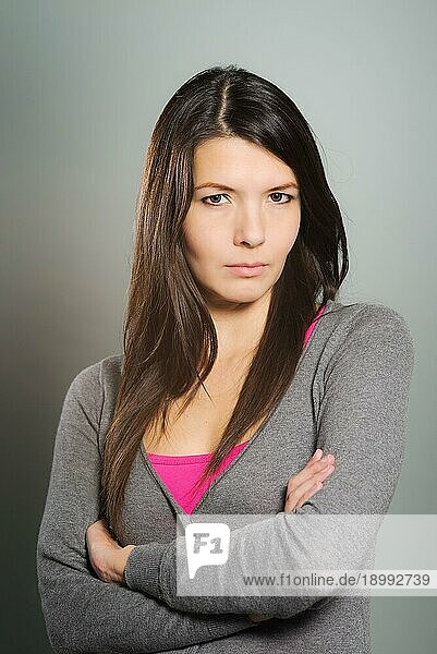 Schwüle  schöne junge Frau mit nach unten geneigtem Kopf  die mit wachsamem  nachdenklichem Blick in die Kamera blickt  vor grauem Studiohintergrund