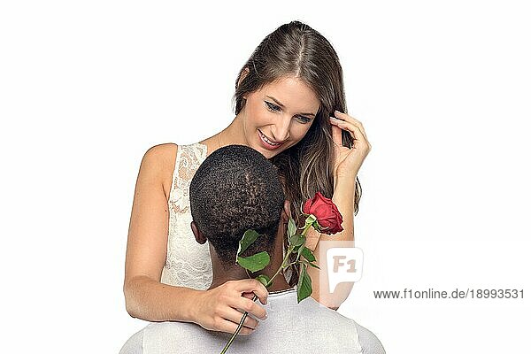 Sentimentale junge Frau  die ihren Freund oder Liebsten umarmt  während sie zärtlich auf eine einzelne rote Rose herablächelt  die er ihr gerade geschenkt hat  symbolisch für Liebe und Romantik oder Valentinstag  gemischtrassiges Paar