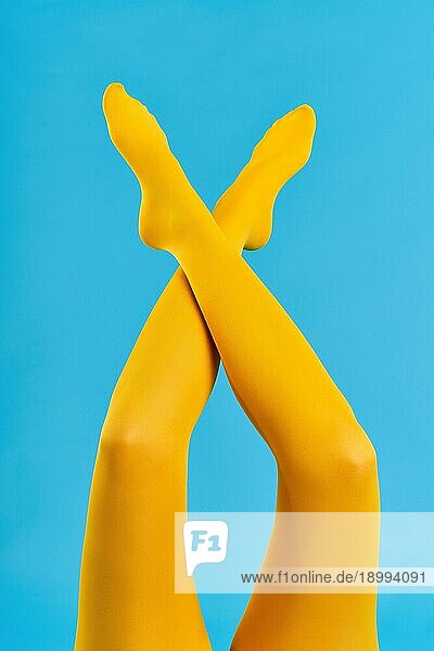 Schlanke weibliche Beine in gelben hellen Strumpfhosen auf blauem Hintergrund erhoben. Entspannen  müde  Gleichgewicht Konzept