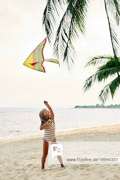 Glückliches kleines Mädchen mit fliegendem Drachen am tropischen Strand unter Palmen. Strand Spaß  glückliche Kindheit Konzept