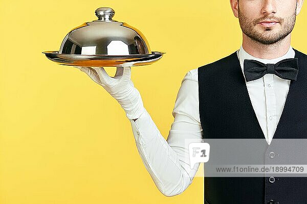 Handsome eleganten Kellner hält Tablett und cloche bereit zu dienen auf gelbem Hintergrund. Service  Restaurant  Horeca Konzept