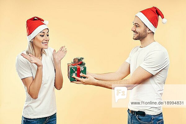 Junger Mann gibt Weihnachtsgeschenkbox an Frau vorbeige Hintergrund. Geschenk  Urlaub  Feier Konzept